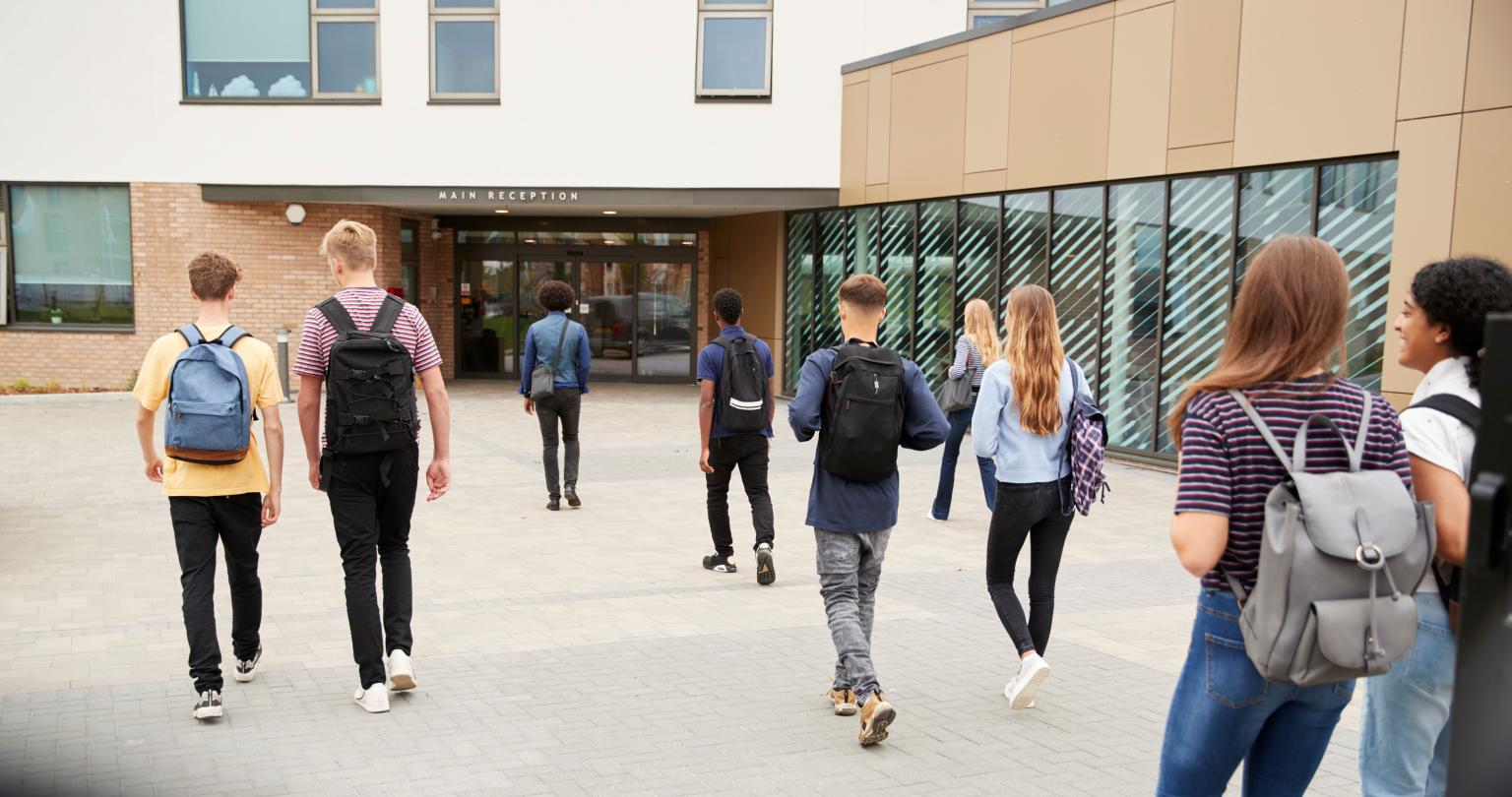 Rear View Of High School Students Walking Into Building Together