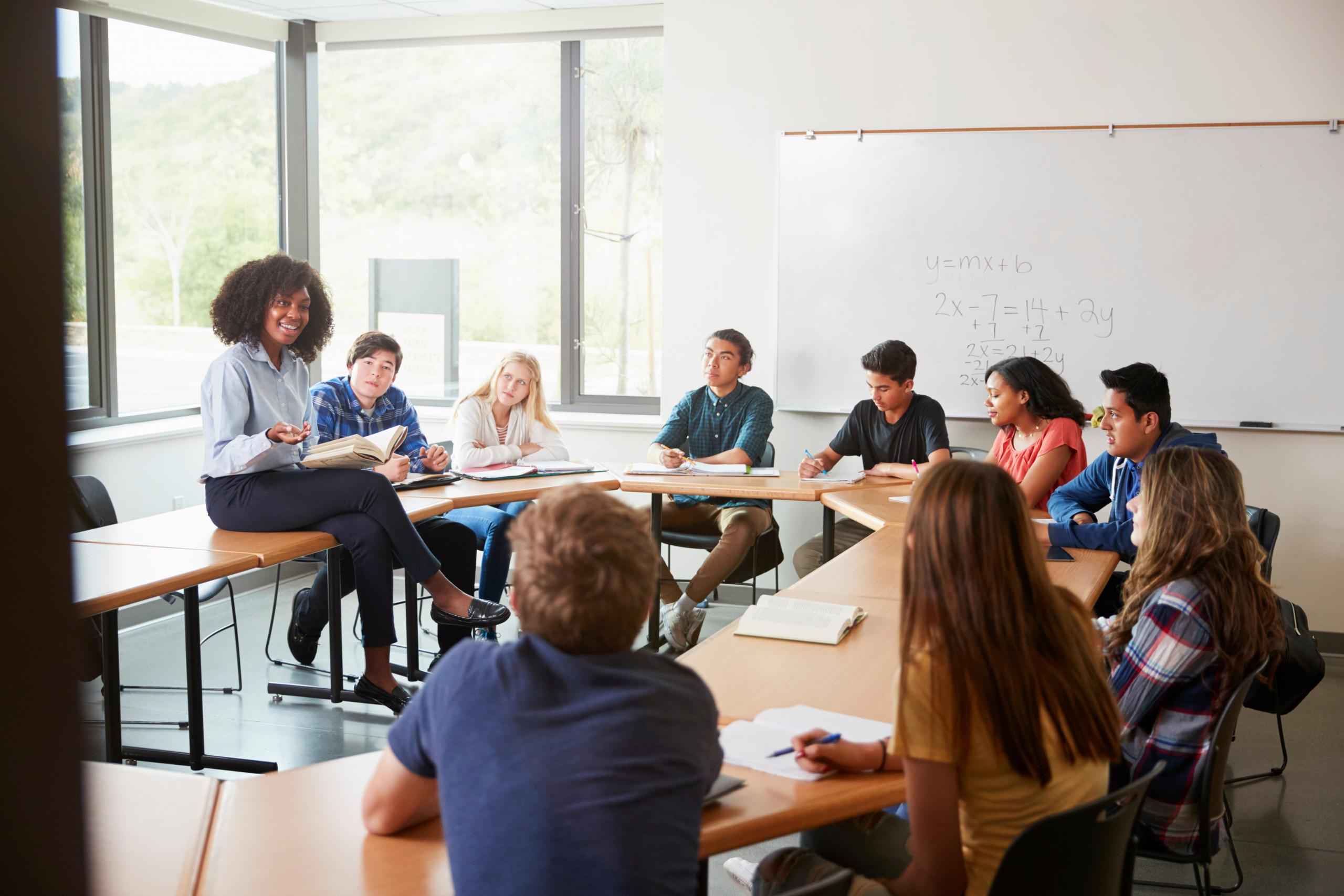 Female High School Tutor Sitting At Table With Pupils Teaching Maths Class