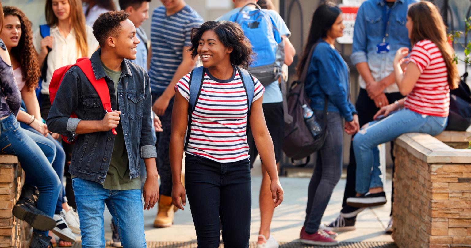 Group Of Smiling Male And Female College Students Walking And Chatting Outside School Building