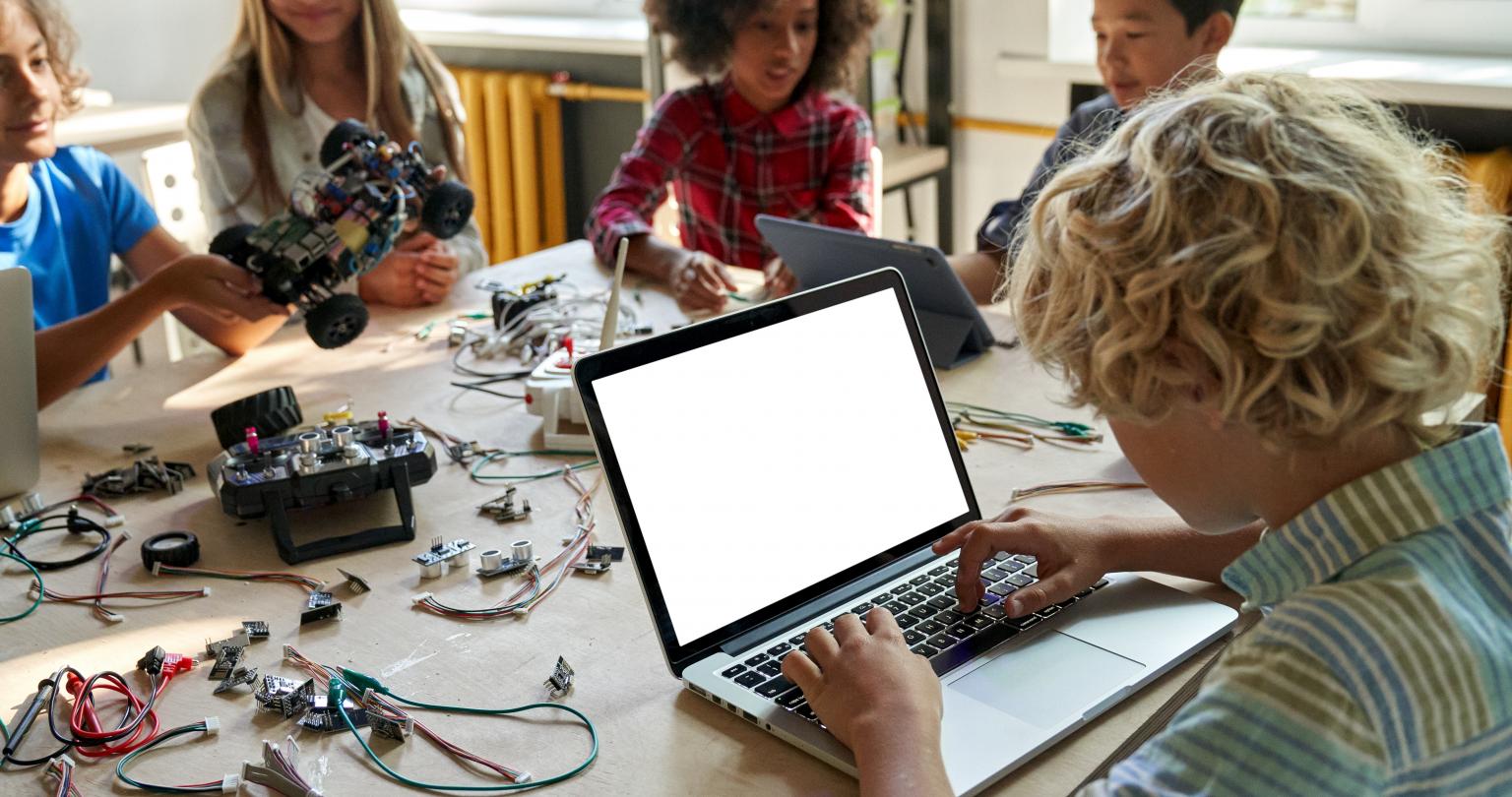 School kid boy using laptop computer with mockup blank empty screen sitting at table during STEM class. Junior school robotics workshop, programming coding robots for students science engineering ads.