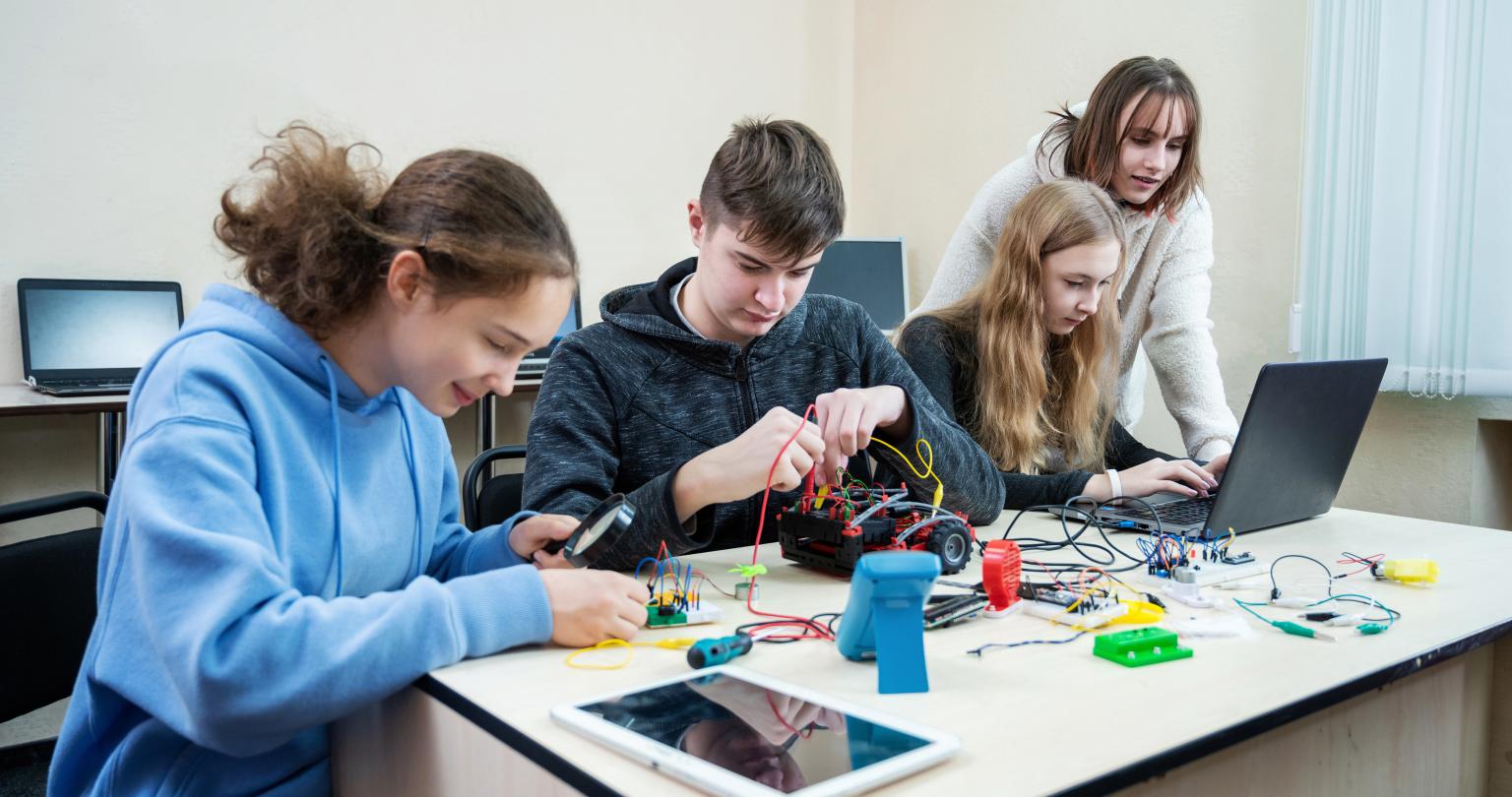 Teenage pupils build robot vehicle learning at table at STEM engineering science education class.