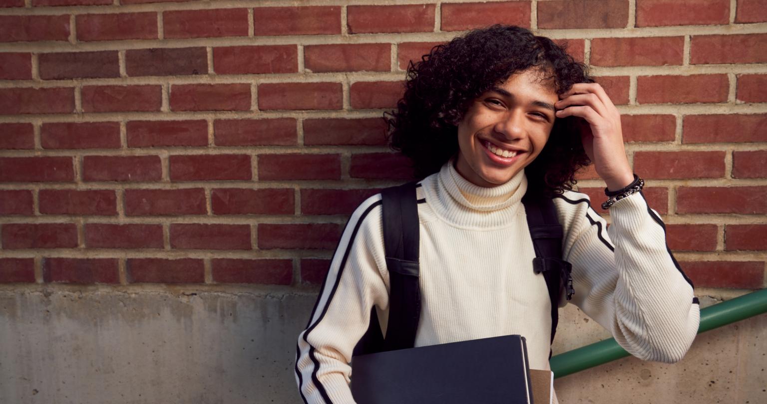 A smiling student standing on stairs wearing a backpack and holding books