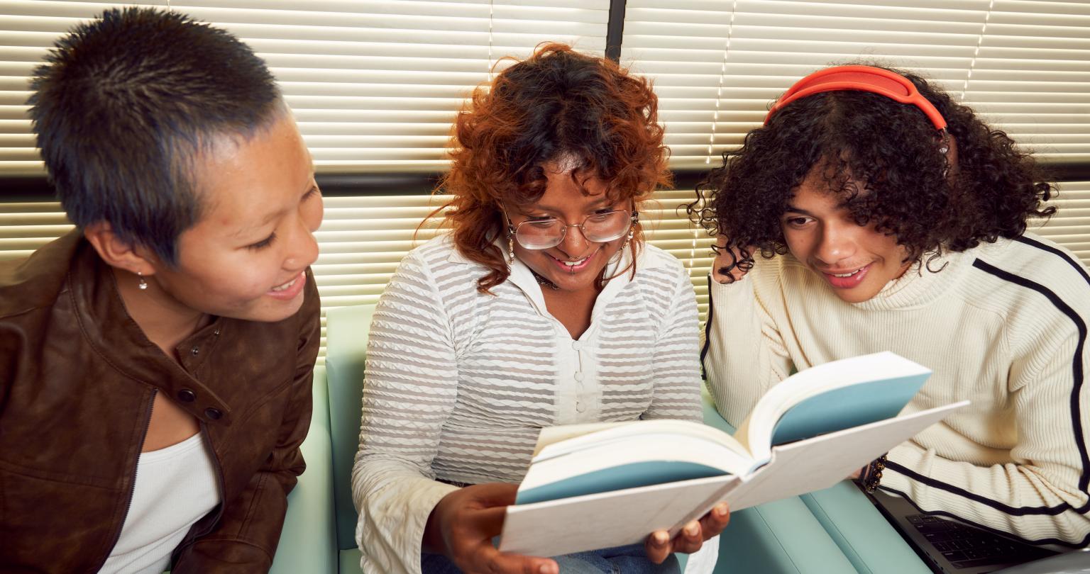 Three girls of different ethnicities sitting together and looking at the same book in the middle