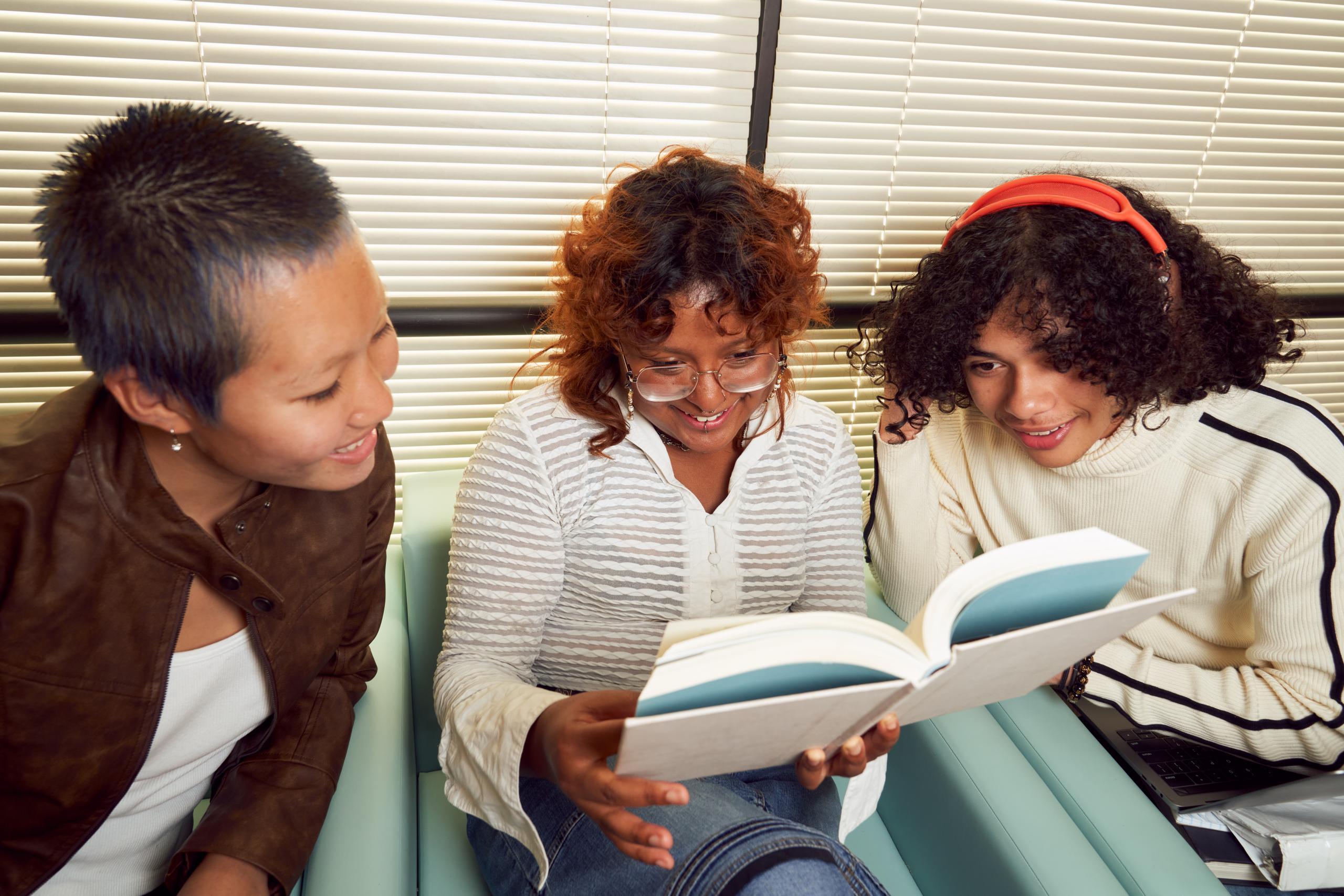 Three girls of different ethnicities sitting together and looking at the same book in the middle