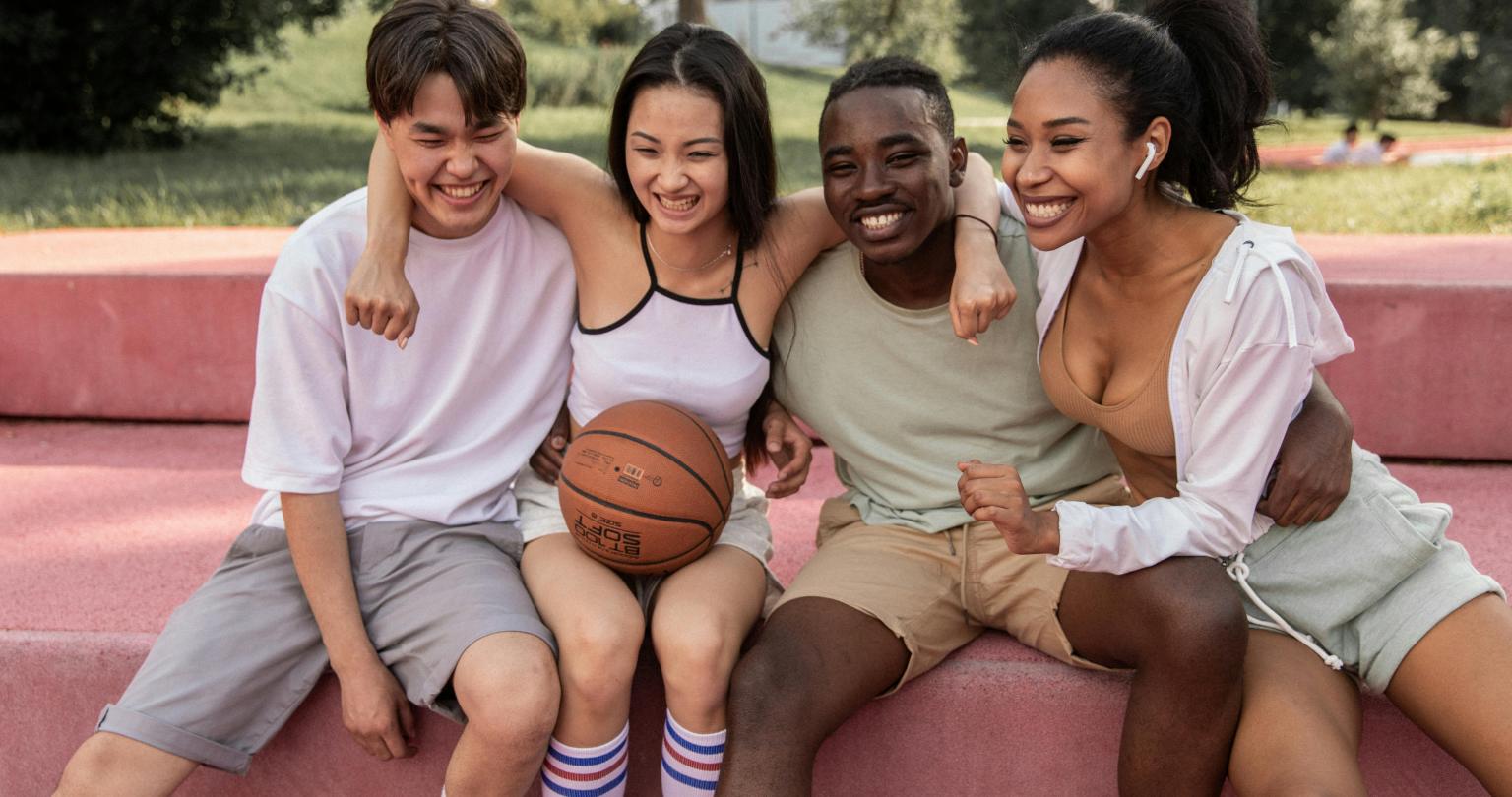 Diverse group of four teenagers dressed in exercise clothing and sitting close to each other.