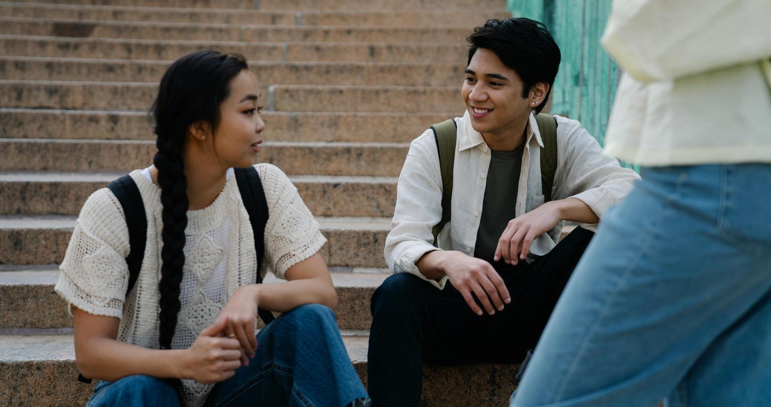 Group of students sitting and standing around stairs talking to each other.