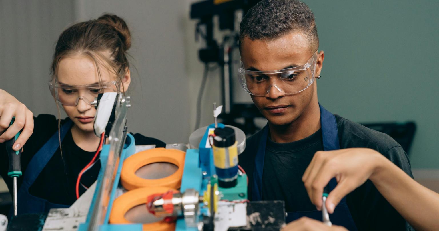 Teenage students wearing safety glasses and working on building a piece of technological equipment.