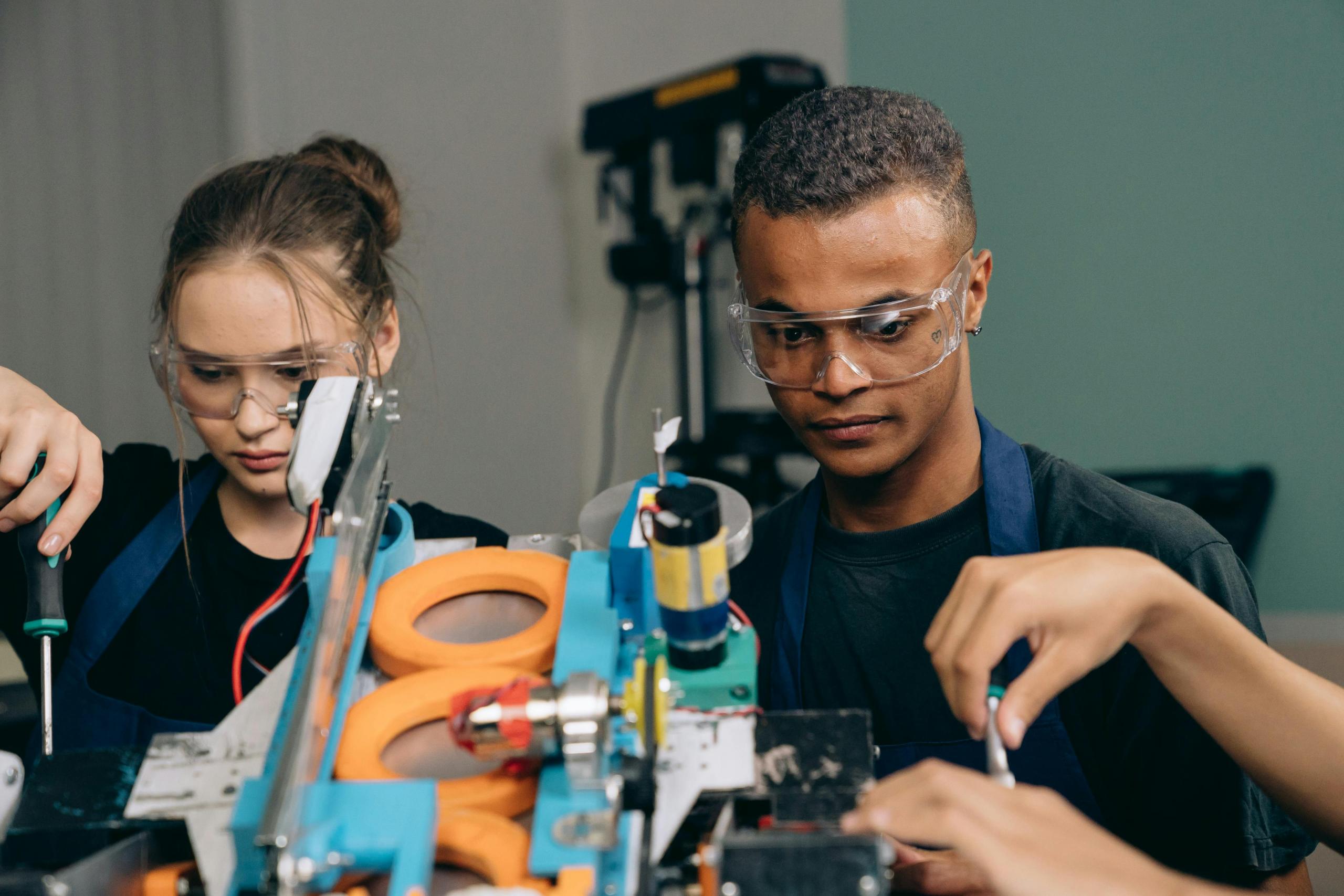 Teenage students wearing safety glasses and working on building a piece of technological equipment.