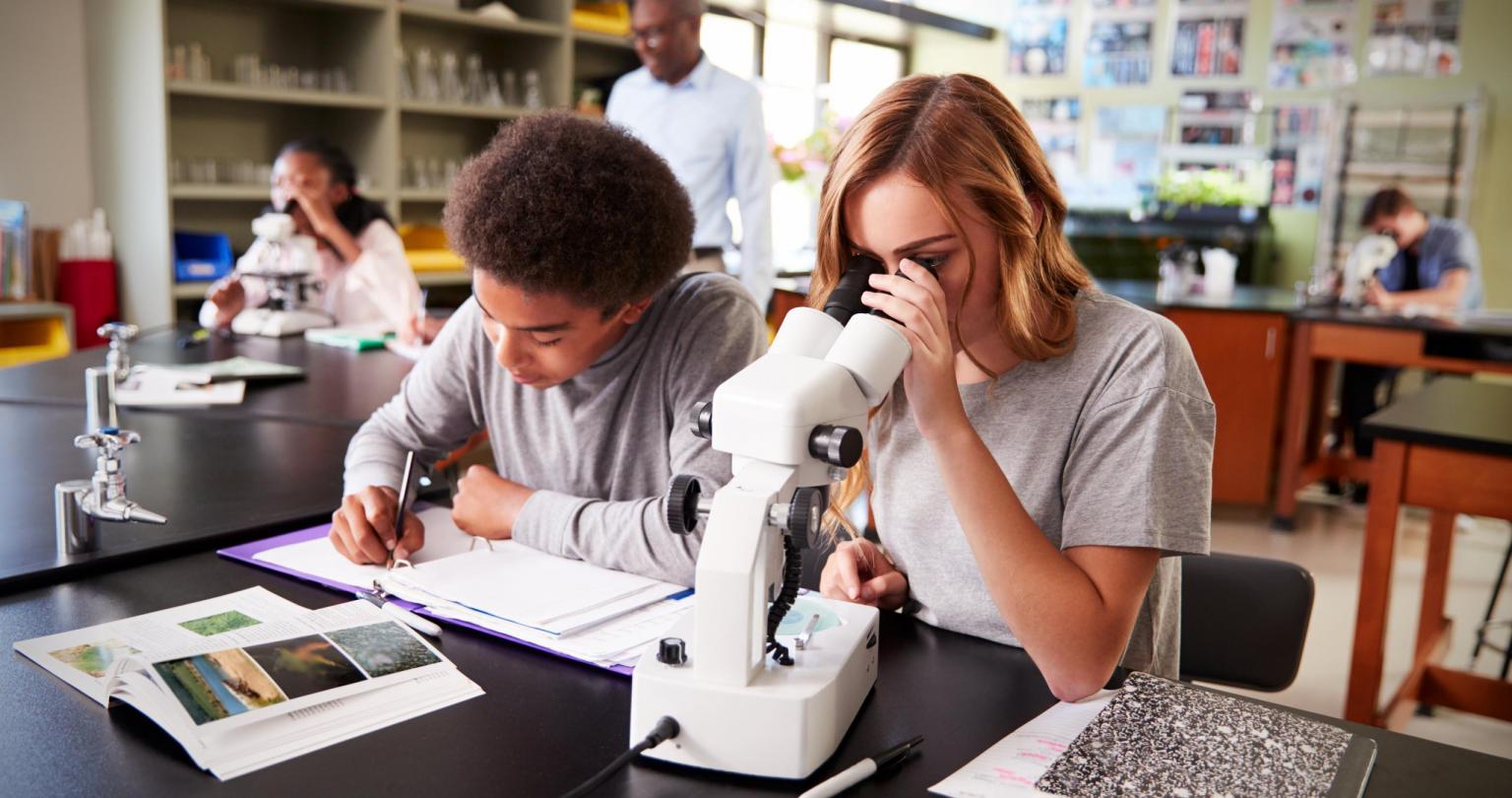 High School Students Looking Through Microscope In Biology Class