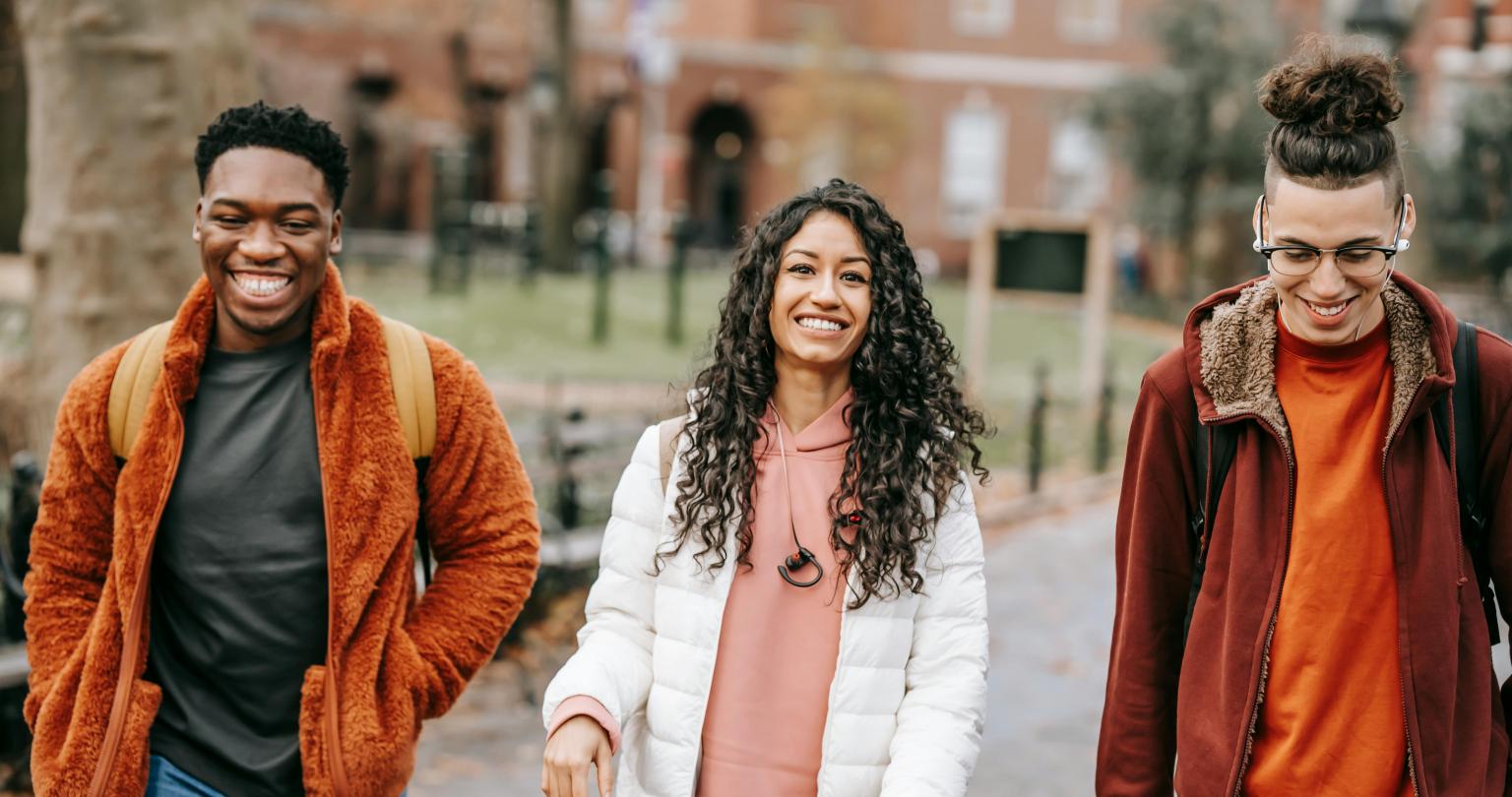 Three young individuals stroll along a sidewalk, enjoying their time together in a lively urban setting.