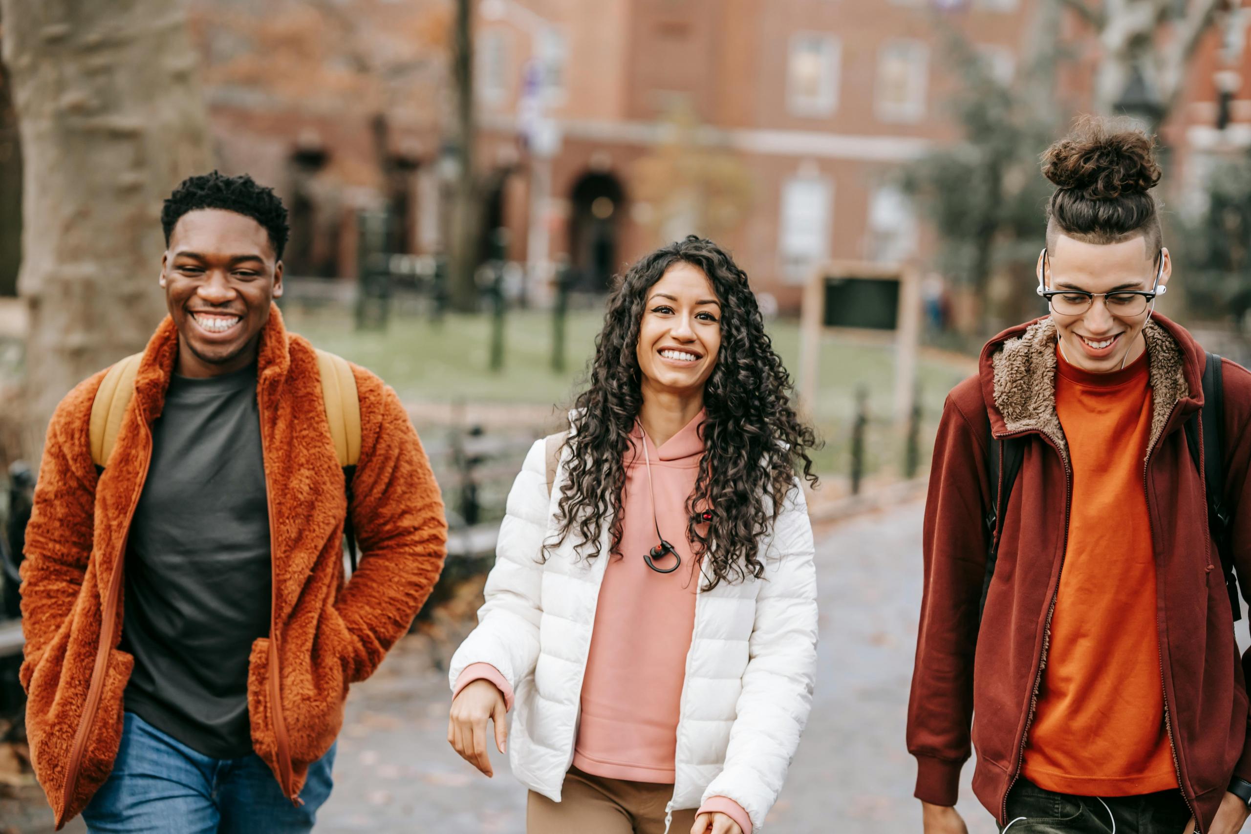 Three young individuals stroll along a sidewalk, enjoying their time together in a lively urban setting.