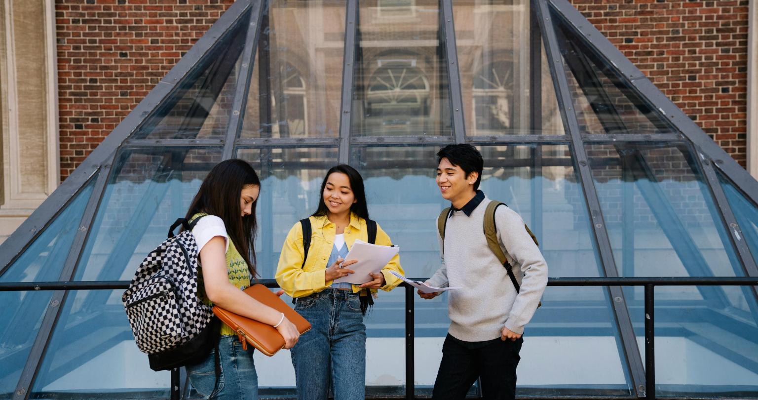 Three school students wearing backpacks standing in front of a building.